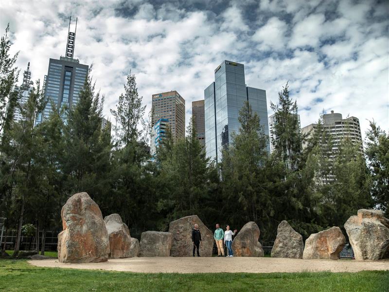 A group of people standing in a park with large rocks and trees.