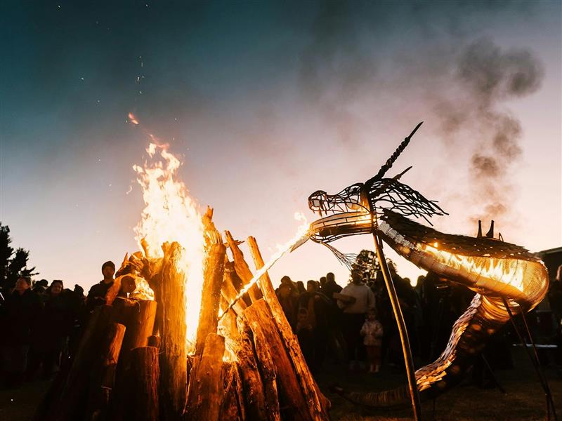 A metal dragon sculpture spits fire onto a bonfire pile