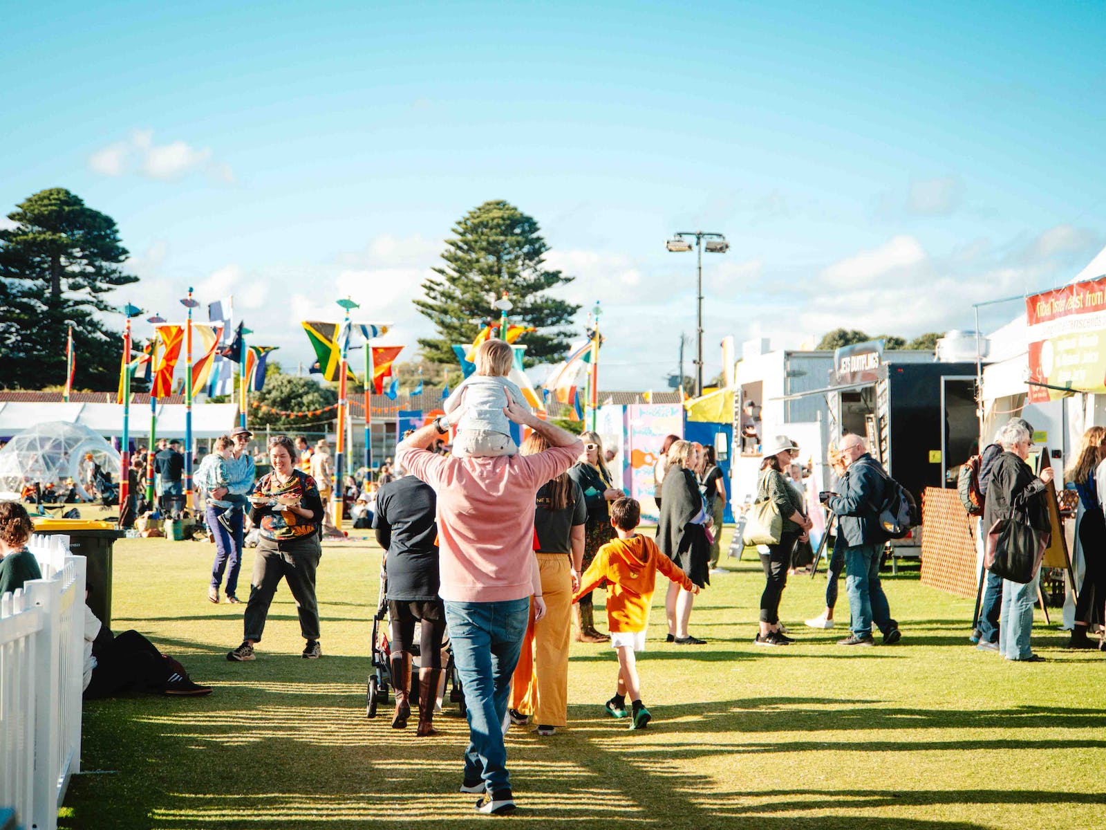 A child on shoulders of an adult at Port Fairy Folk Festival. The sky is very blue.