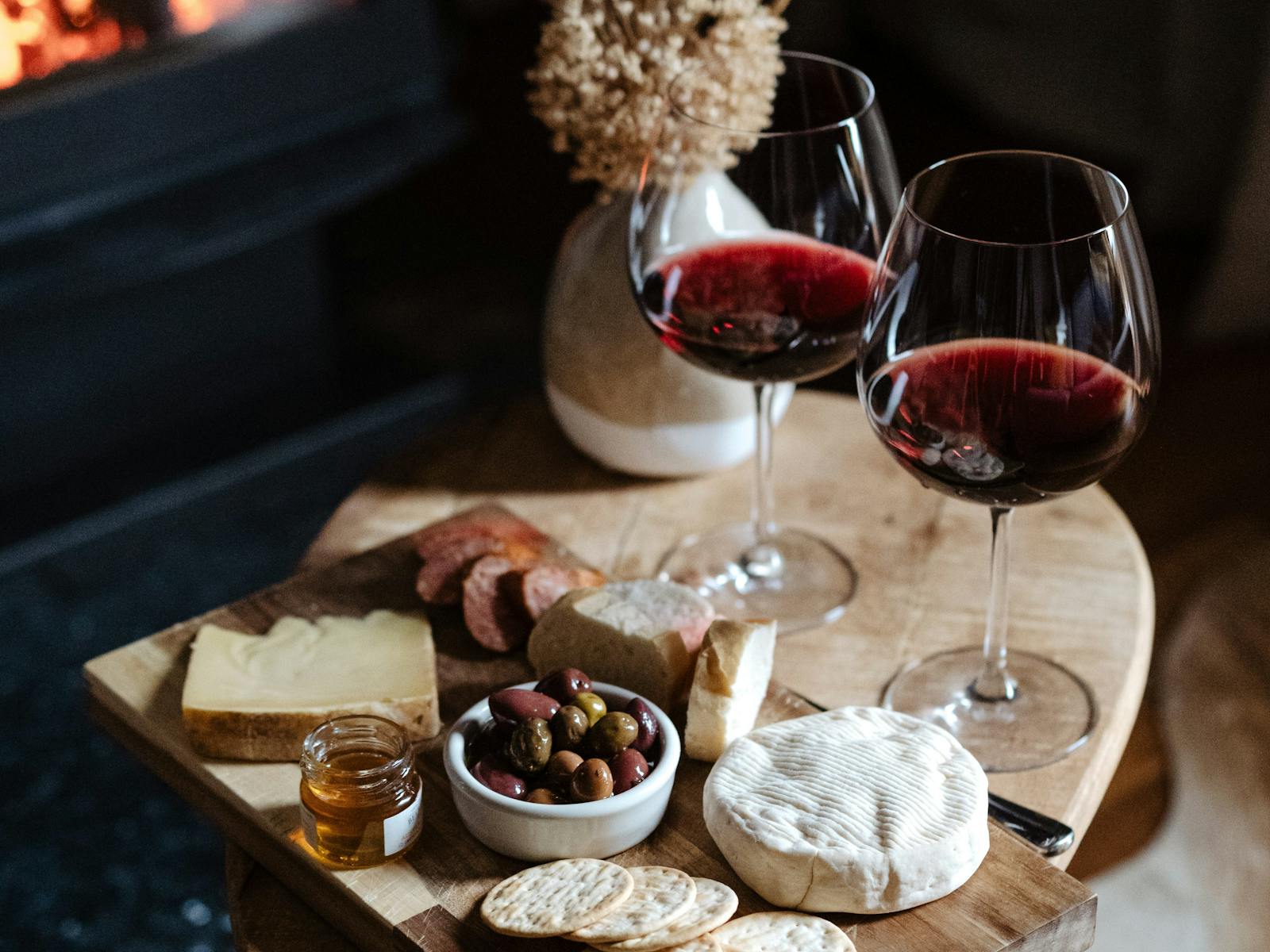 A cheese board using local ingredients with red wine infront of a fire