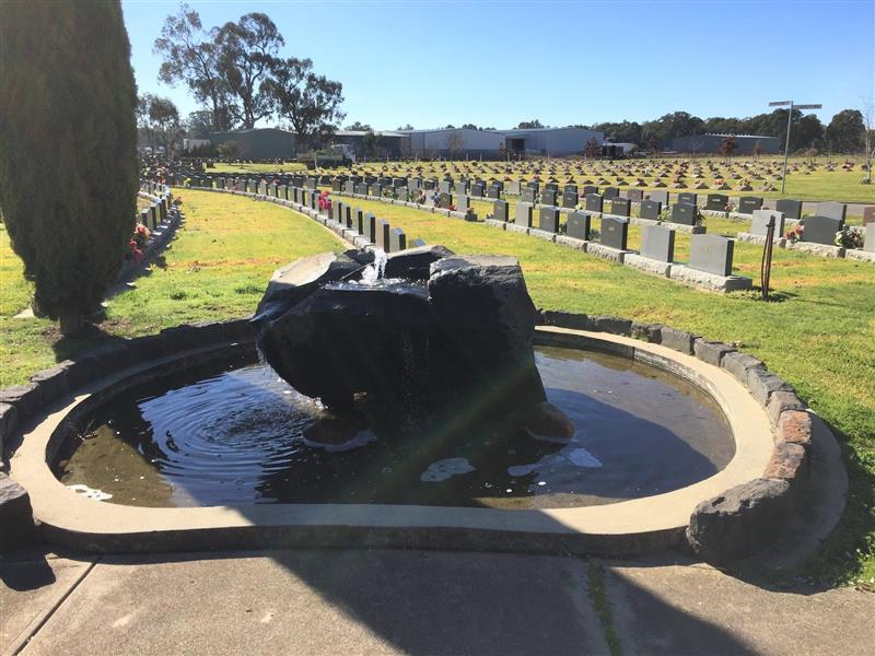 Memorial Fountain in the lawn part of the cemetary with lines of headstones in background