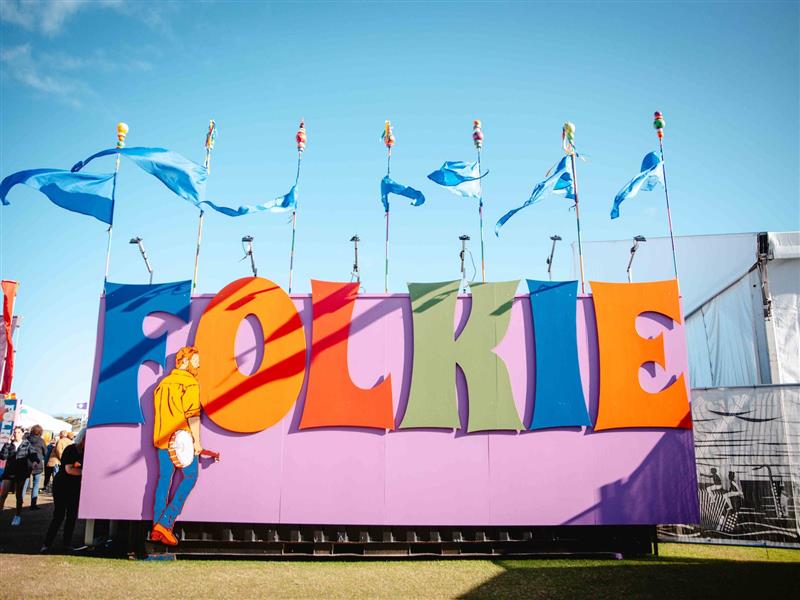 Artwork displaying the word  "Folkie" and a man with a banjo inside the Port Fairy Folk Festival.