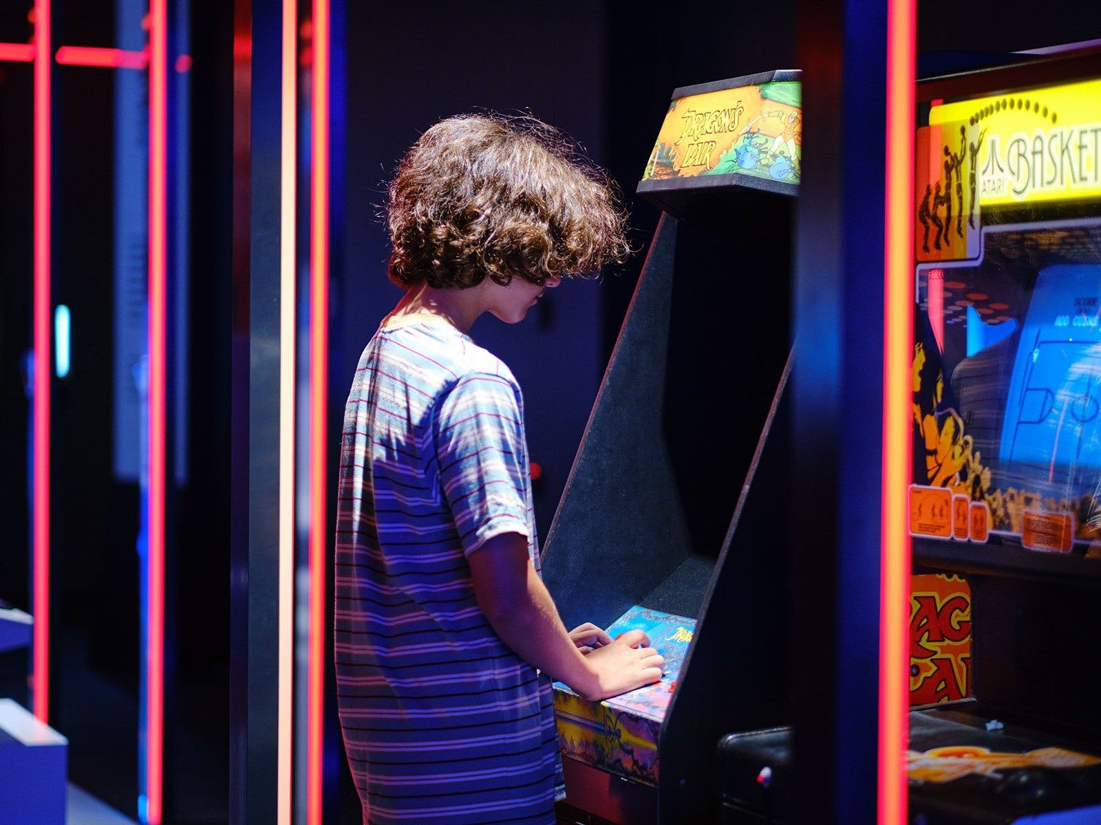 boy standing in front of arcade game with neon lights