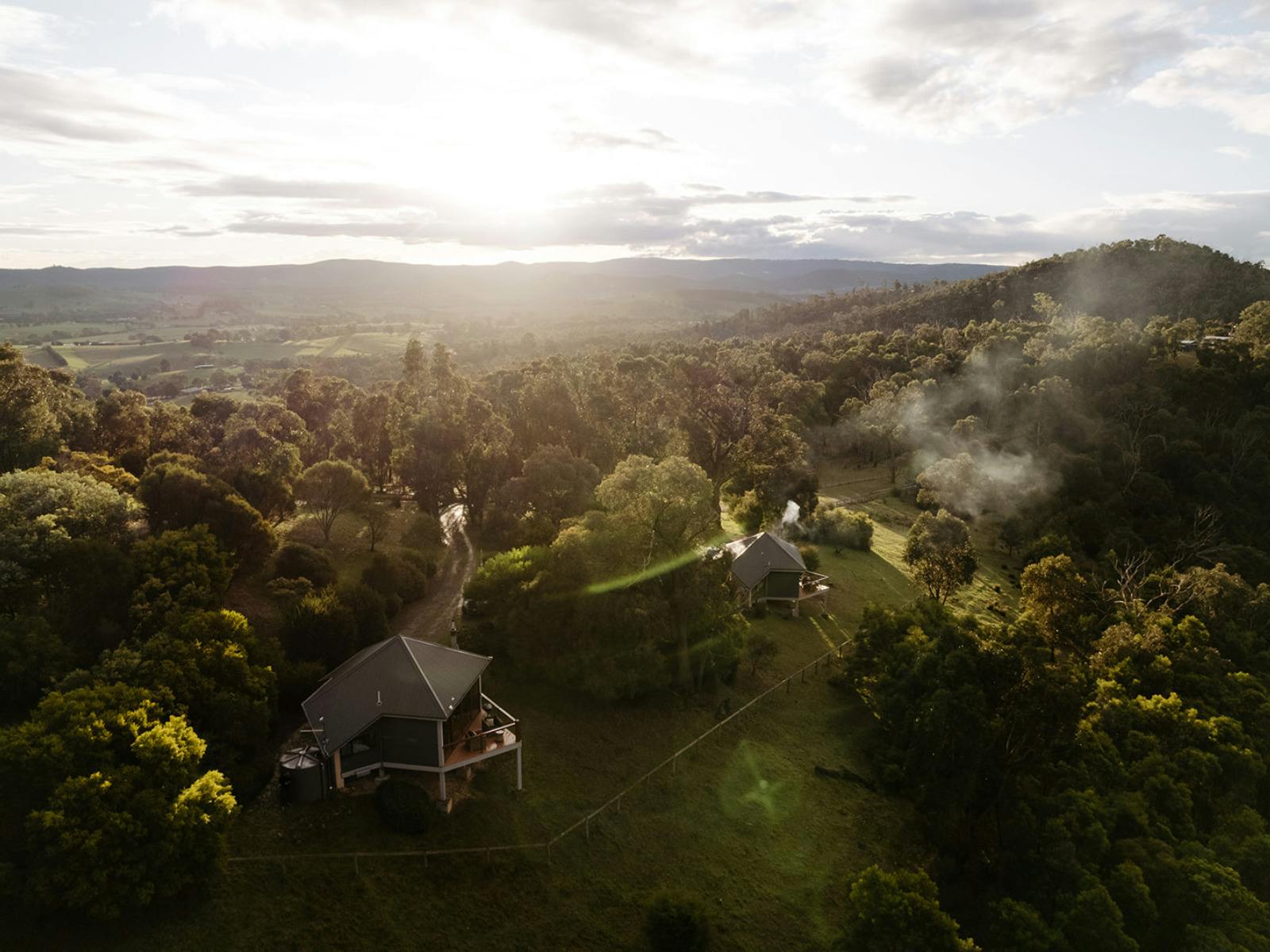 Two mudbrick cabins perched on the east side of a ridge line with the sunsetting in the background